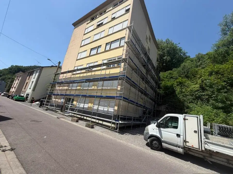 Immeuble de cinq niveaux en bord de rue, échafaudage sur la façade latérale et premiers panneaux isolants posés en partie basse.