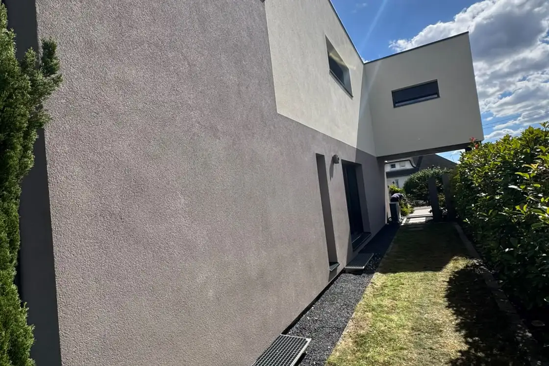 Entrée et accès au garage d’une maison contemporaine, enduit de finition clair sur les volumes et gris en soubassement.