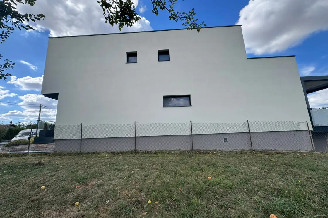 Façade arrière d’une maison contemporaine revêtue d’un enduit de finition clair, baies vitrées et menuiseries anthracite.