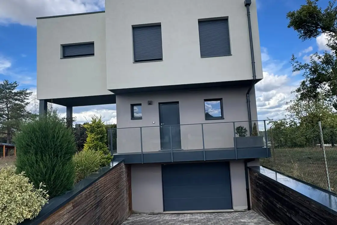 Façade de maison contemporaine côté rue, enduit de finition clair et menuiseries anthracite.