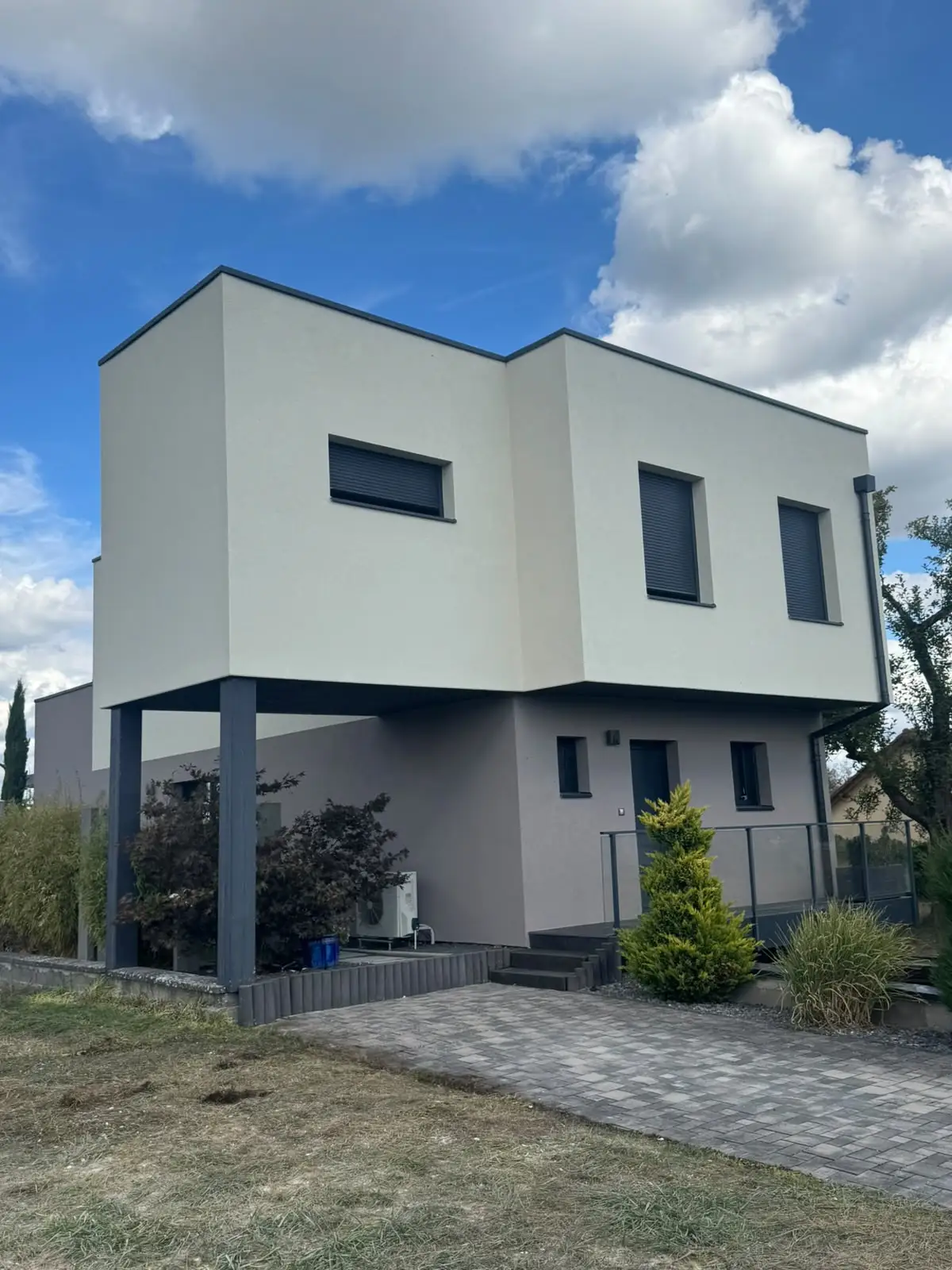 Angle rentrant de la maison, grandes surfaces d’enduit blanc cassé à l’étage, niveau inférieur en enduit gris clair.