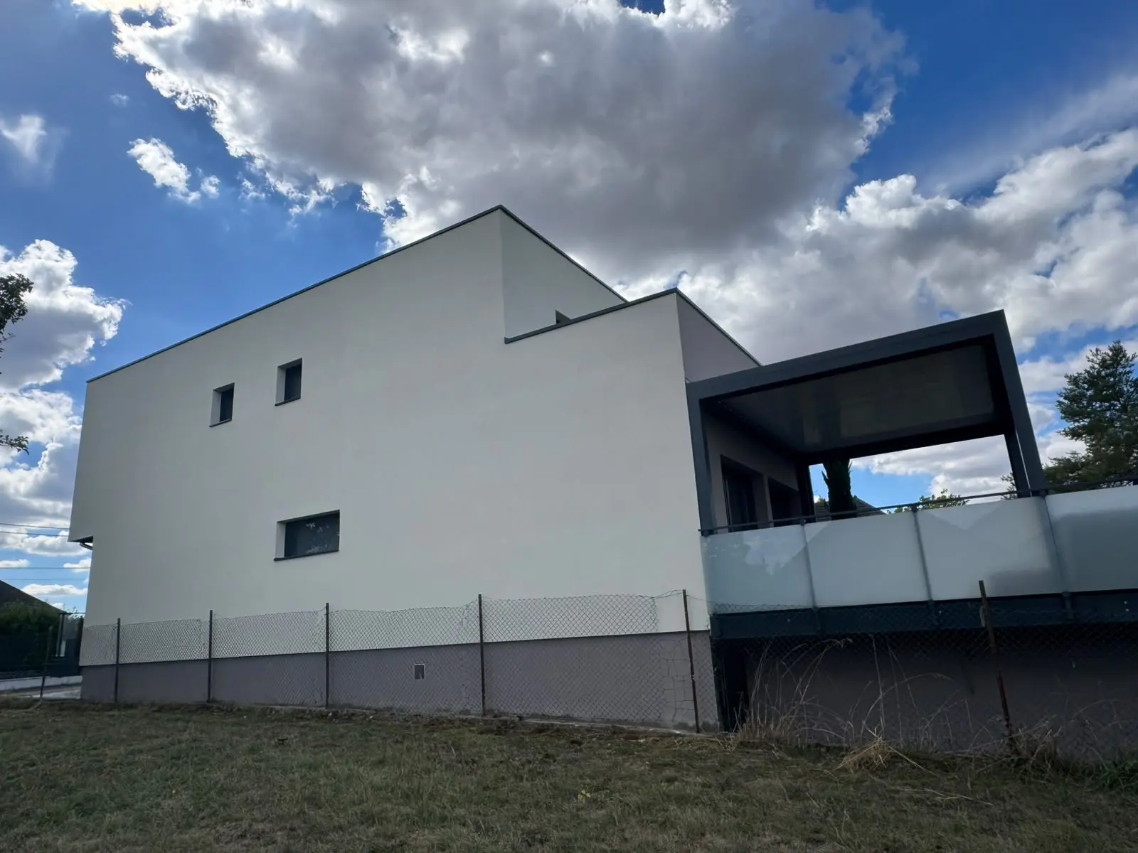 Pignon de maison contemporaine recouvert d’un enduit de finition blanc cassé, menuiseries sombres.