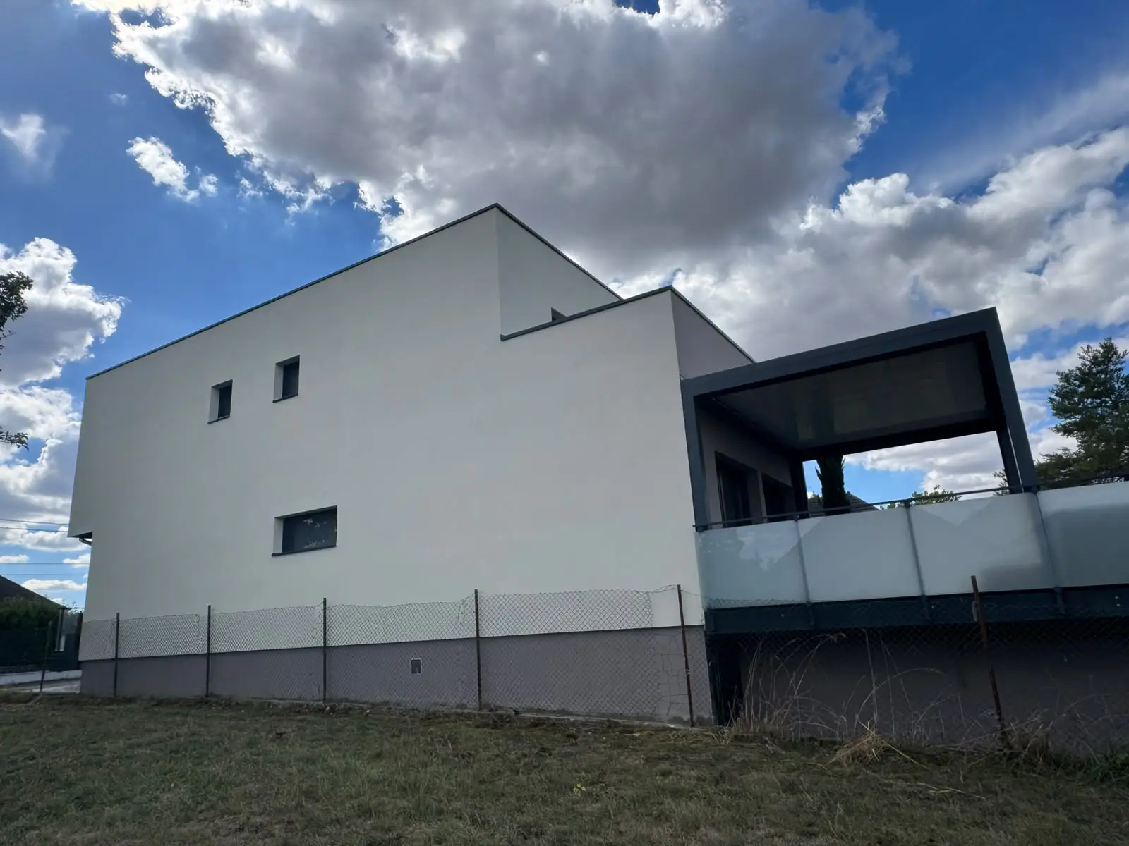 Pignon de maison contemporaine recouvert d’un enduit de finition blanc cassé, menuiseries sombres.