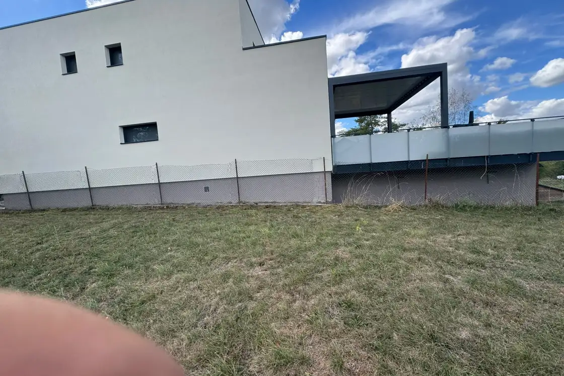 Pignon d’une maison contemporaine vu du jardin, mur extérieur en enduit de finition clair.