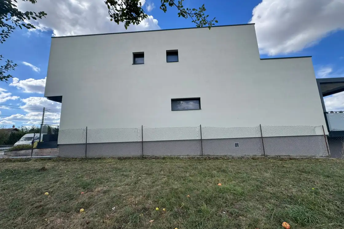 Façade de maison contemporaine avec balcon sur pilotis métalliques et enduit de finition clair.