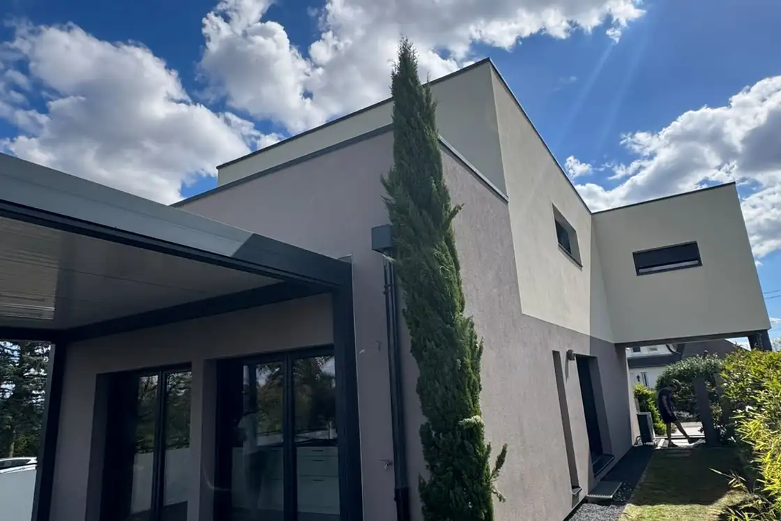 Terrasse sous pergola d’une maison contemporaine, murs extérieurs en enduit de finition clair.