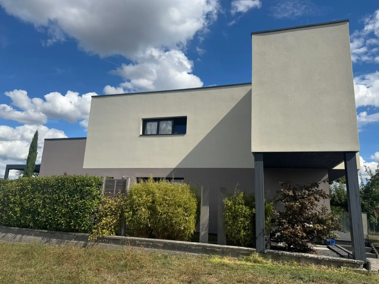 Maison contemporaine vue depuis le jardin, enduit de finition en deux teintes claires et volumes décalés.