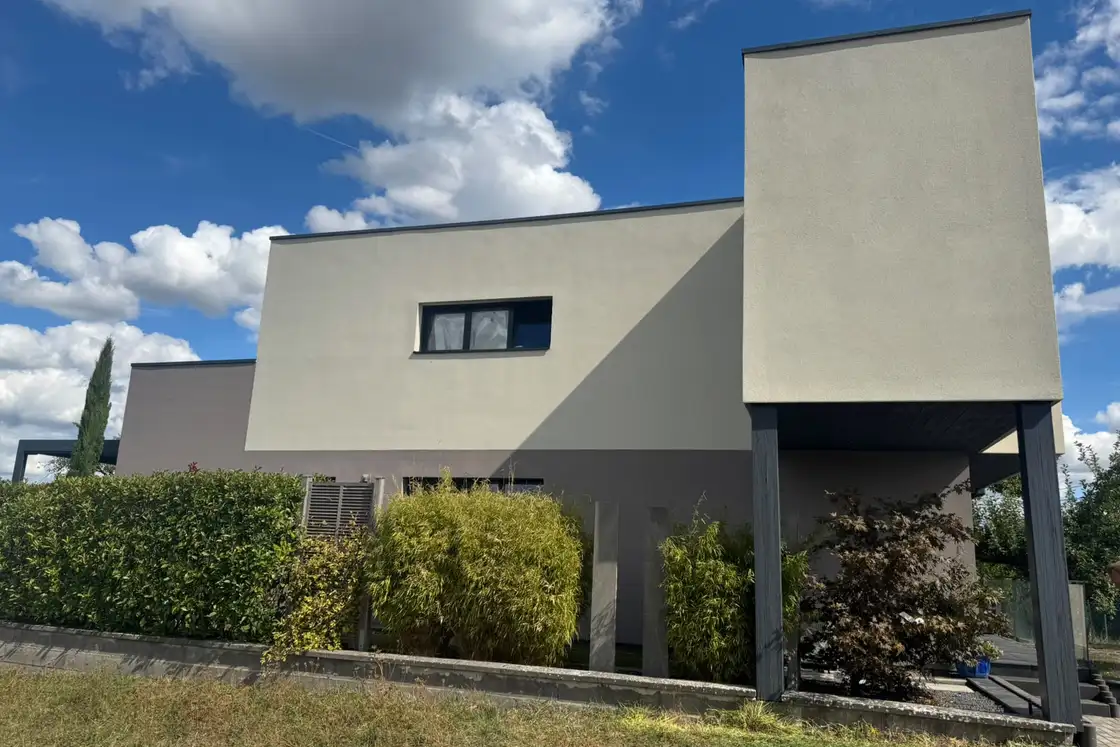 Maison contemporaine vue depuis le jardin, enduit de finition en deux teintes, claire sur les volumes et grise en soubassement.