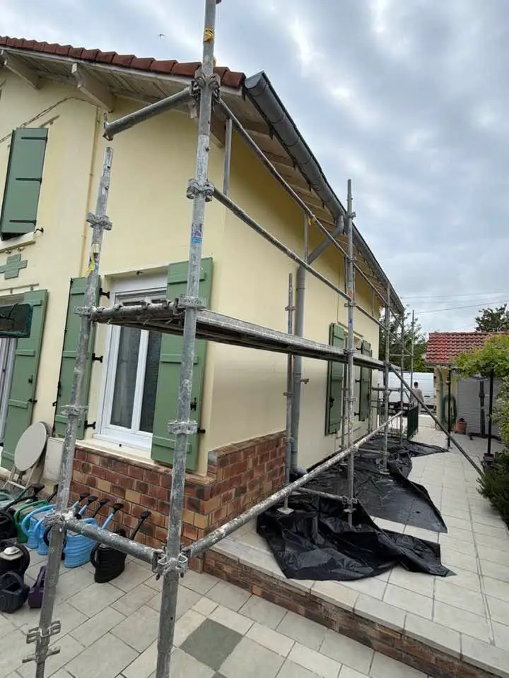 Maison sous échafaudage, bâches noires déroulées sur la terrasse et autour des plantations.