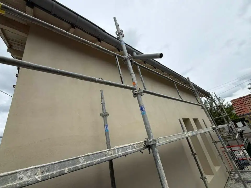 Façade couverte d’un sous-enduit beige appliqué sur l’isolant, échafaudage en place.