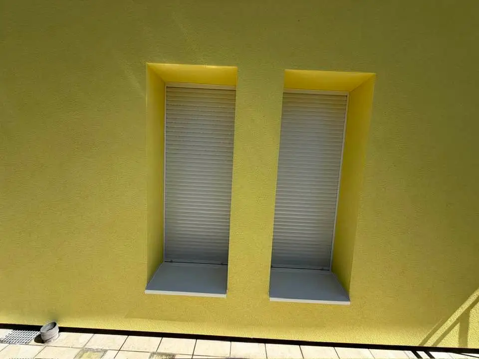 Détail de deux fenêtres à volets roulants, tableaux enduits en jaune et appuis repris.