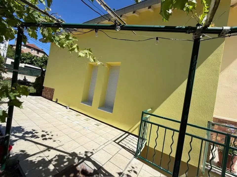 Vue de la façade terminée en enduit jaune depuis la terrasse carrelée, sous une treille.